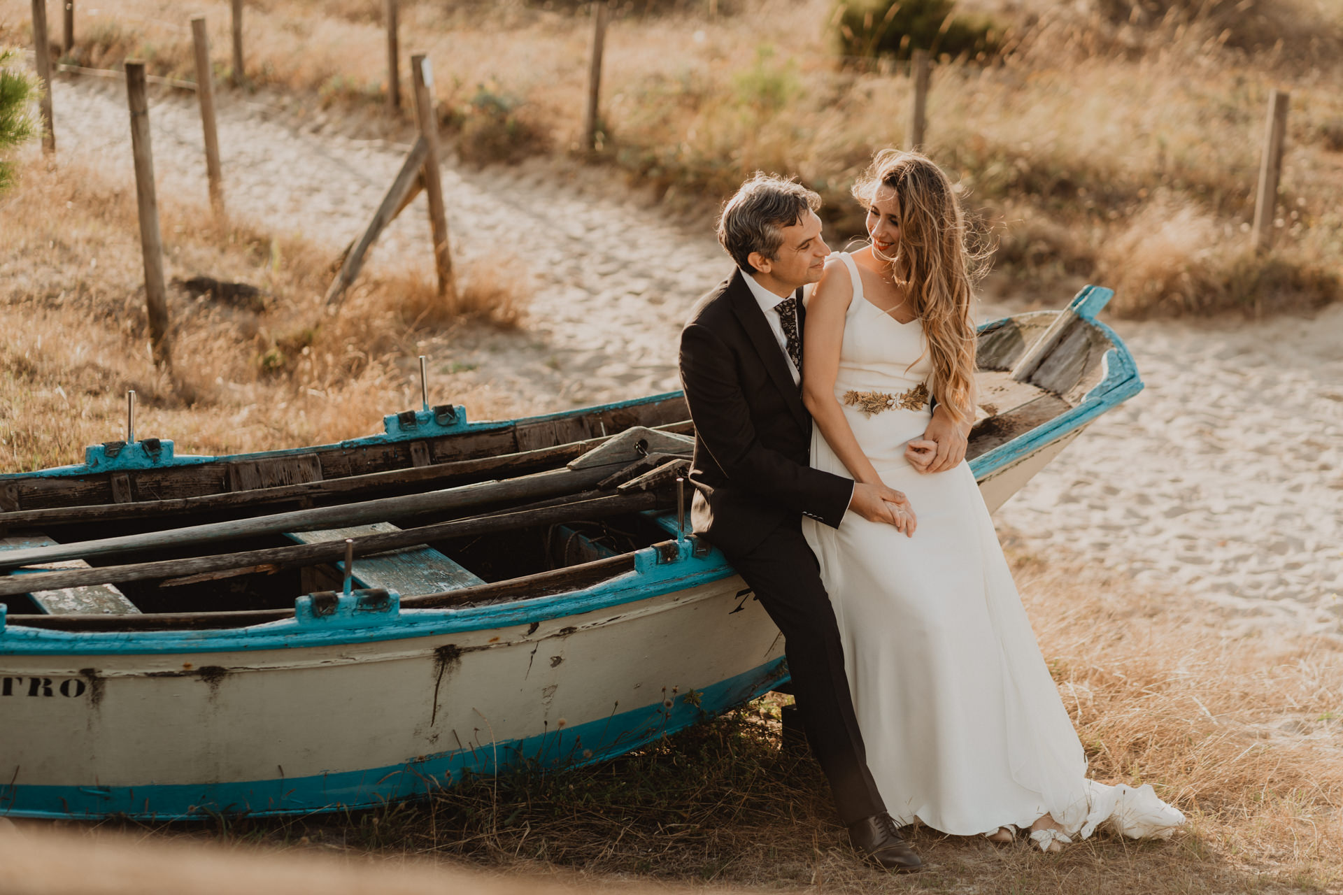 Pareja de recien casados en una playa sobre un barco de madera